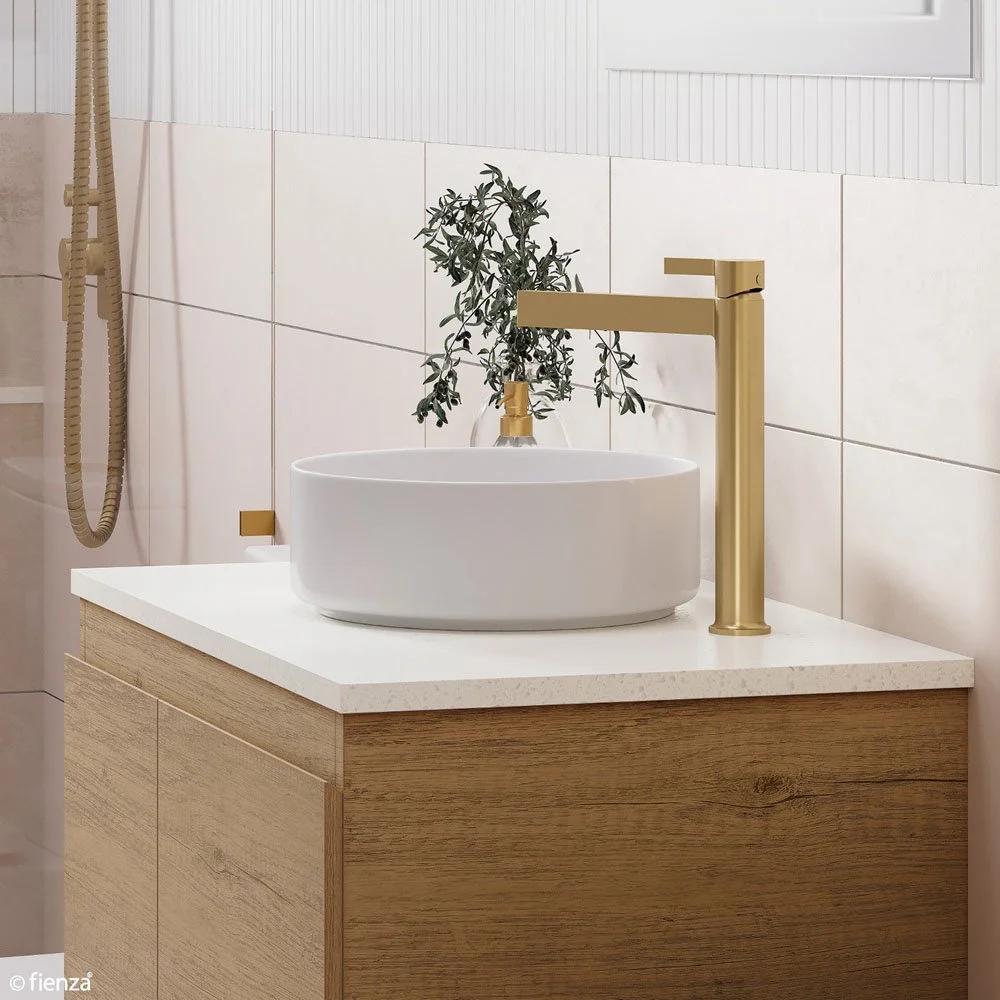 Bathroom vanity with a modern white vessel sink, gold faucet, and a potted plant, against a tiled wall.
