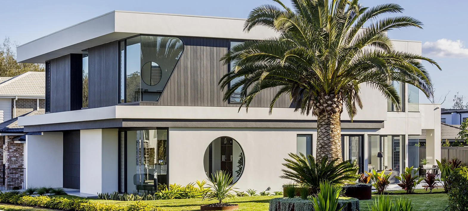 Modern two-story house with white and dark exterior, large windows, and a palm tree in the front yard.