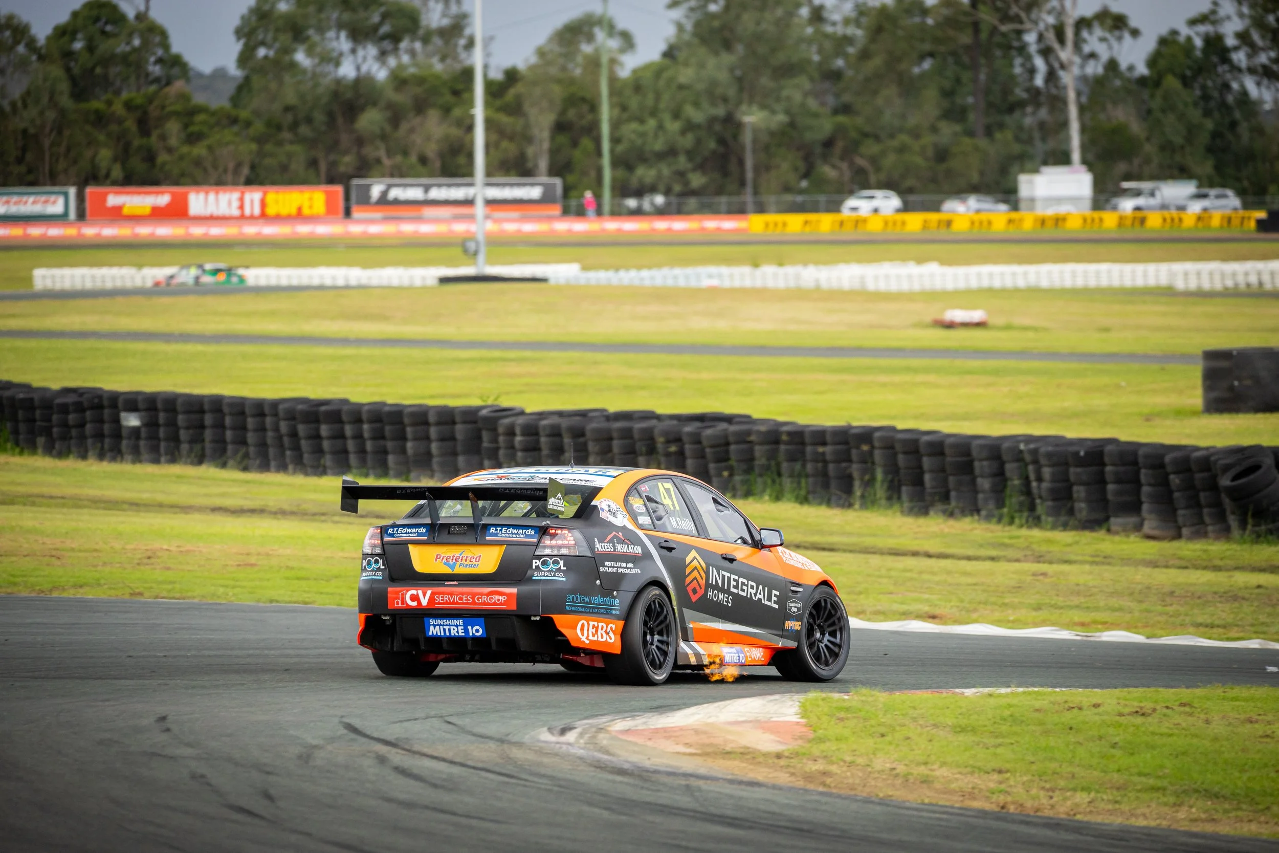 Race car on a track, turning a corner at a motorsport race, with tire barriers and advertisements in the background.