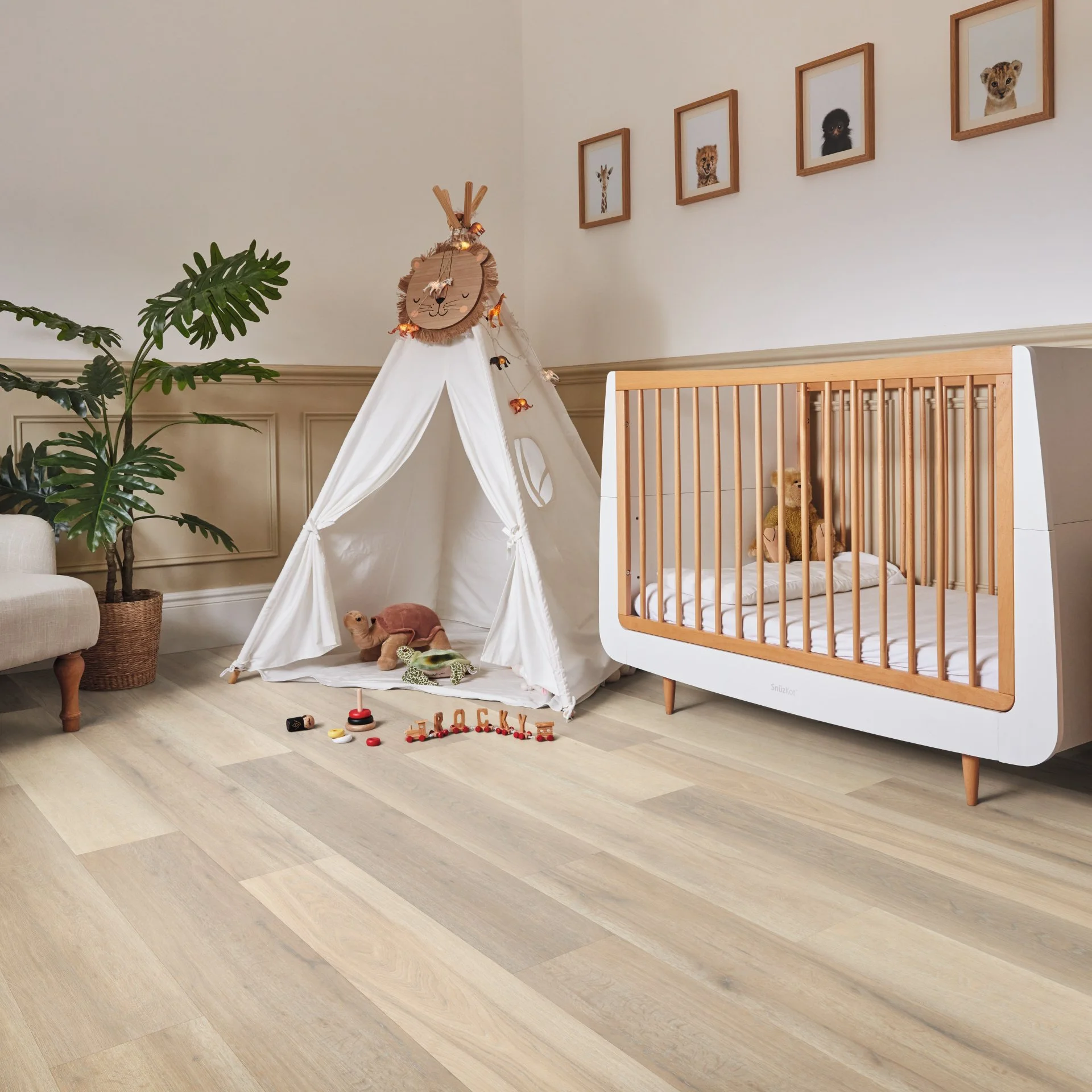Nursery room with a play tent, plush toys, and a crib, decorated with framed animal pictures on the wall and a large green plant.