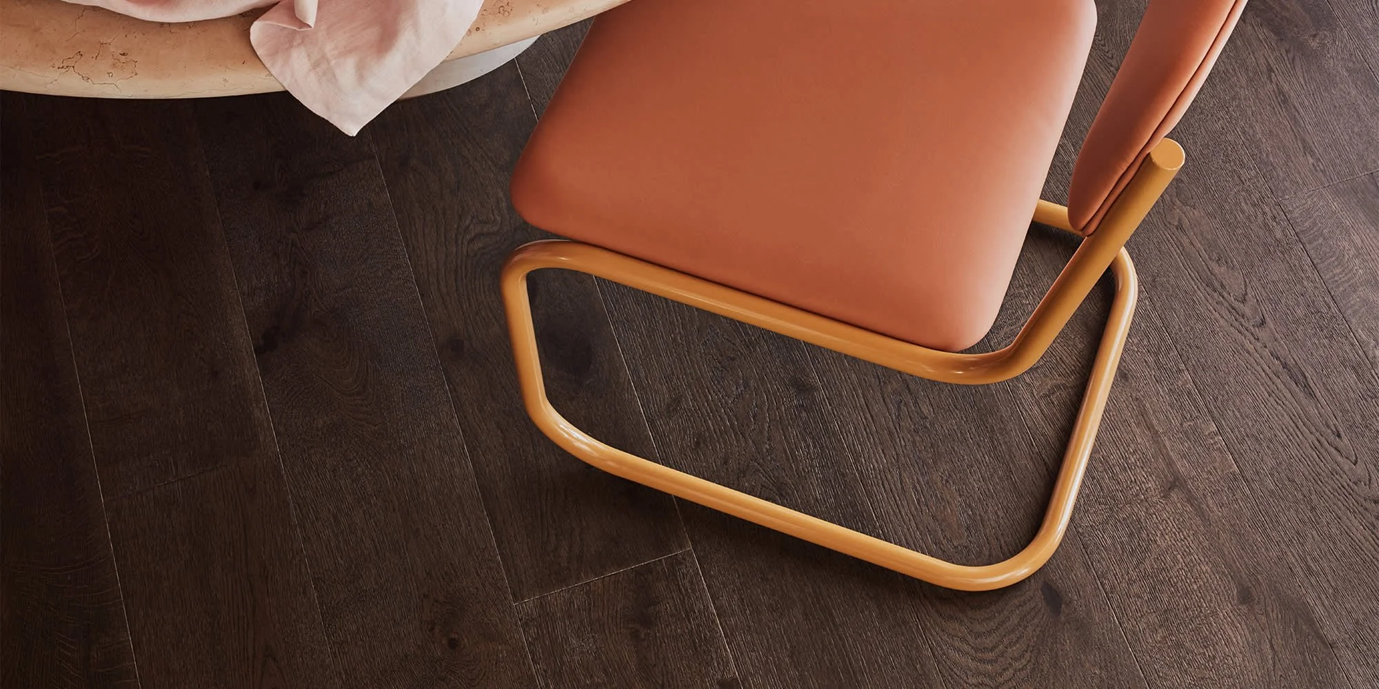 Top view of a pink chair with wooden frame on a dark wooden floor near a marble table with a cloth
