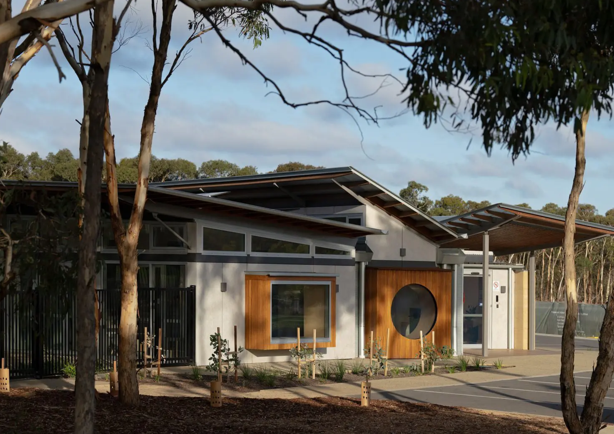 Modern building with angular metal roof, wooden accents, surrounded by trees and parking lot
