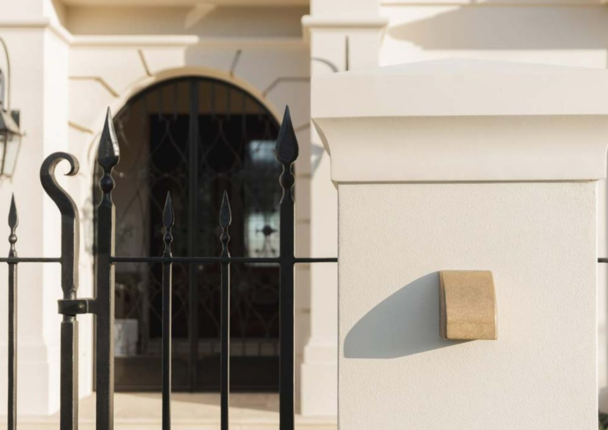 Close-up of a white wall with a mailbox and a black wrought iron fence.