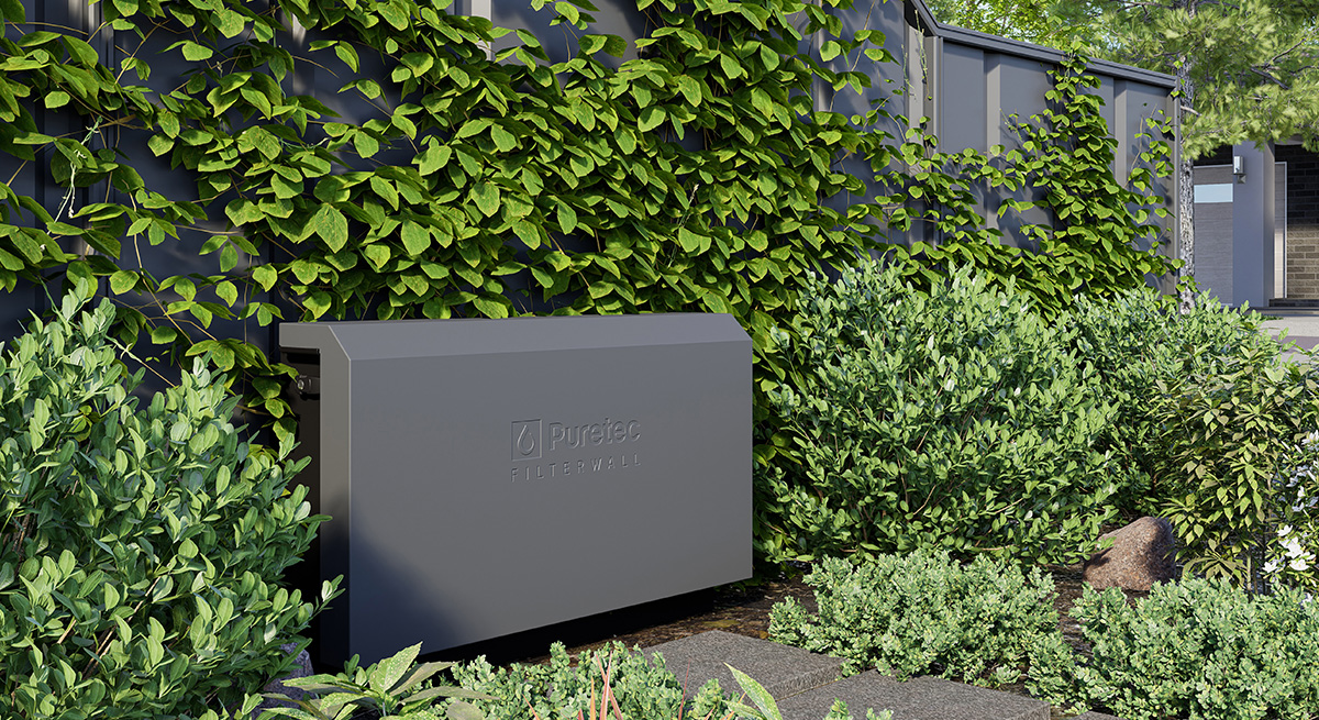 A gray Puretec Filterwall unit installed outdoors among green bushes and climbing plants.