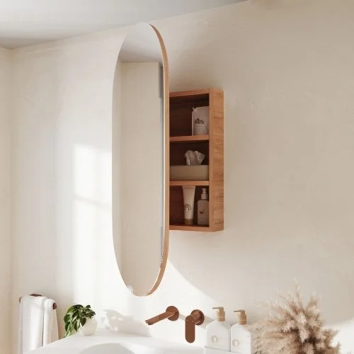 Bathroom with a wooden framed oval mirror, a wooden shelf with toiletries, and a white faucets with soap dispensers.