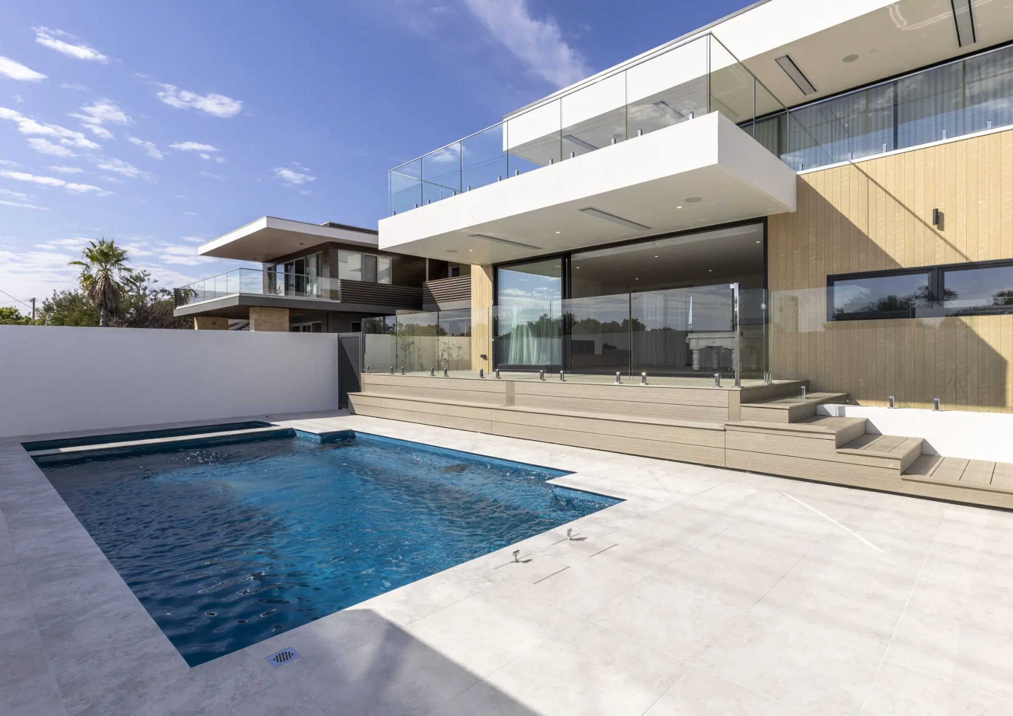 Modern house with large glass windows and a pool in the backyard on a sunny day.