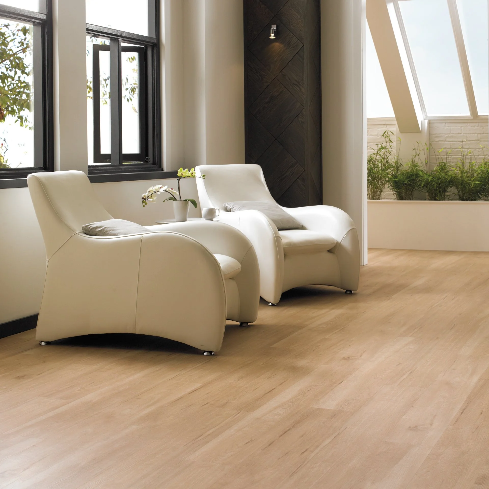 Modern living room with two white leather chairs, a small table with a potted orchid, large black-framed windows, and a corner with green plants on a windowsill.