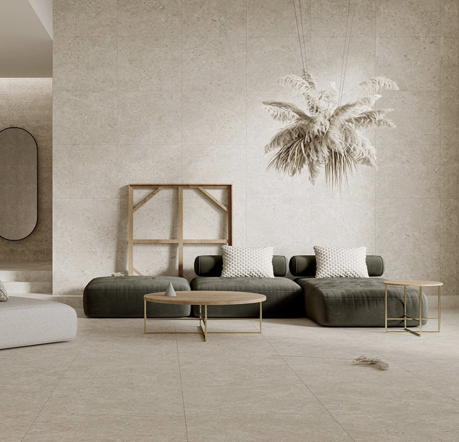 Minimalist living room with beige tiled floor and wall, black sofa with white pillows, small round coffee tables, and a large hanging pampas grass arrangement.