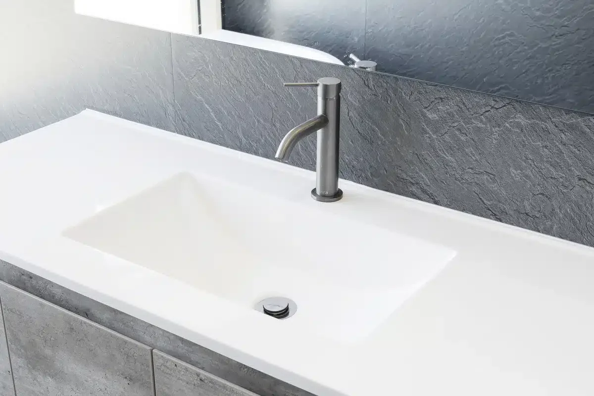 Modern bathroom sink with a silver faucet, mounted on a stone countertop, with a mirror above reflecting part of the sink.
