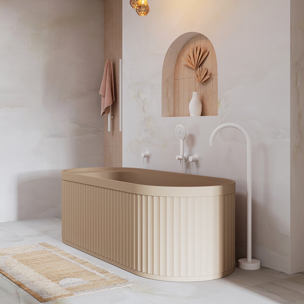 Modern bathroom with a beige freestanding bathtub, white wall-mounted showerhead, and a curved white floor lamp. Beige towel hangs on a hook, and decorative dried leaves in a niche with a white vase.