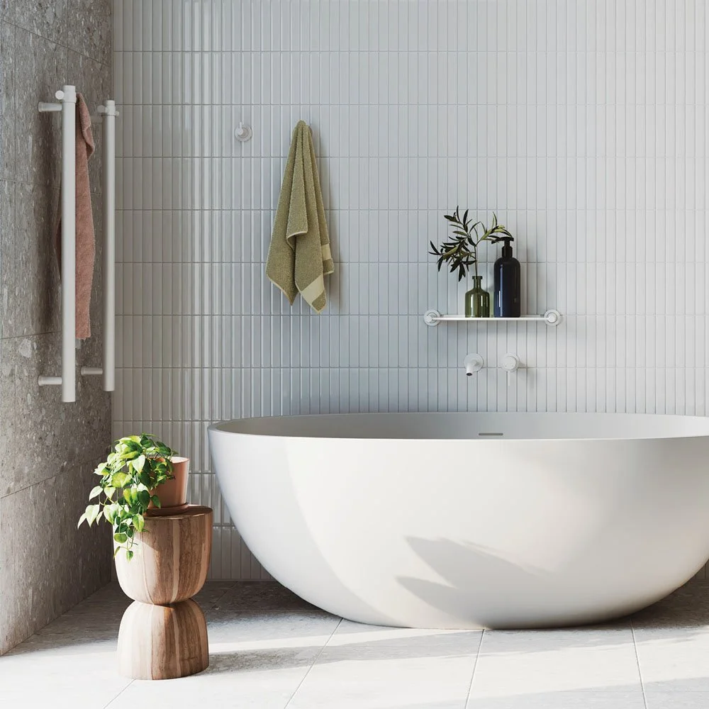 Modern bathroom with a white freestanding bathtub, potted plant on a wooden stand, and minimalistic decor including towels and vases on a wall shelf.