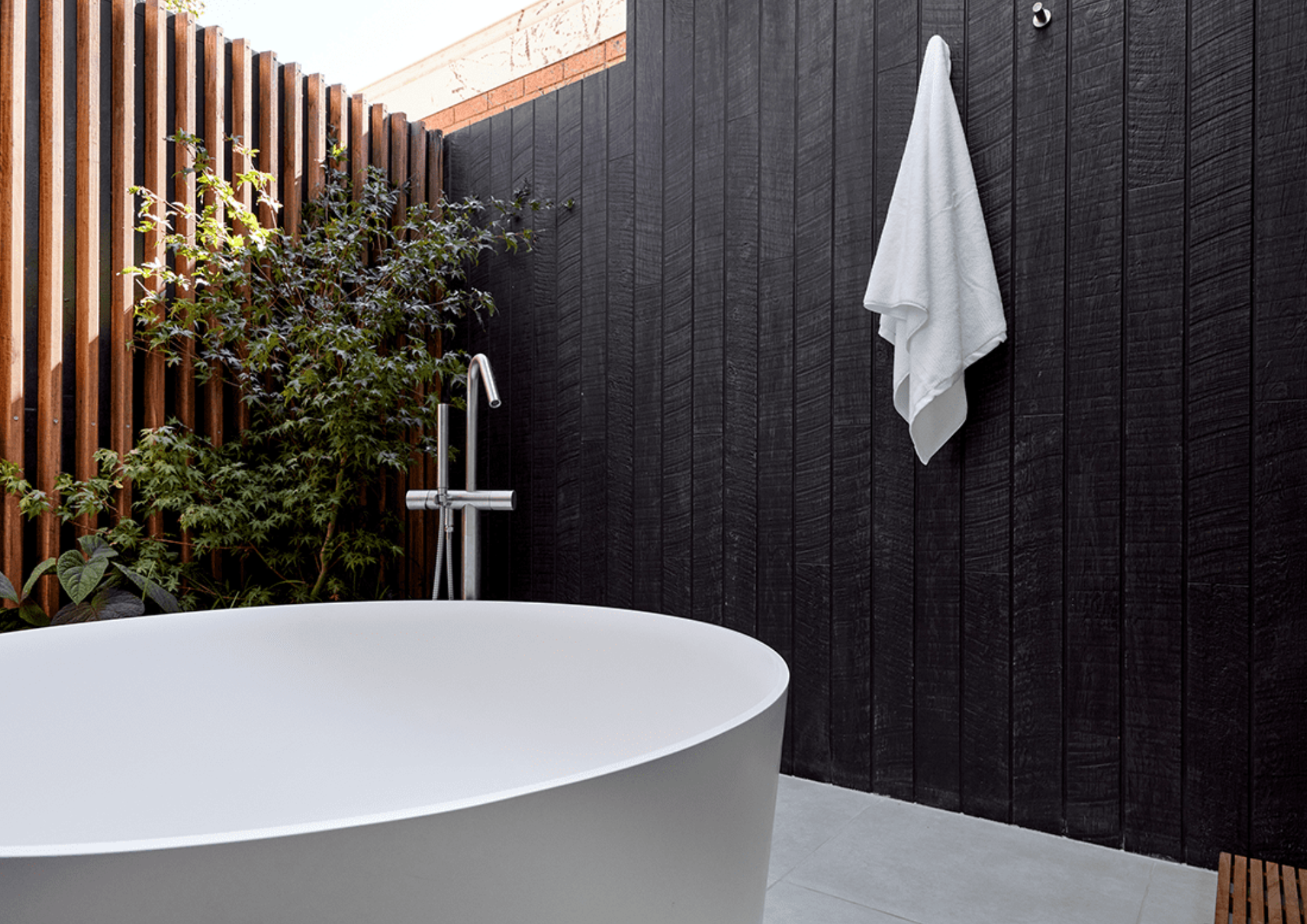 Outdoor bathtub with a black wooden fence and a white towel hanging on the black wall