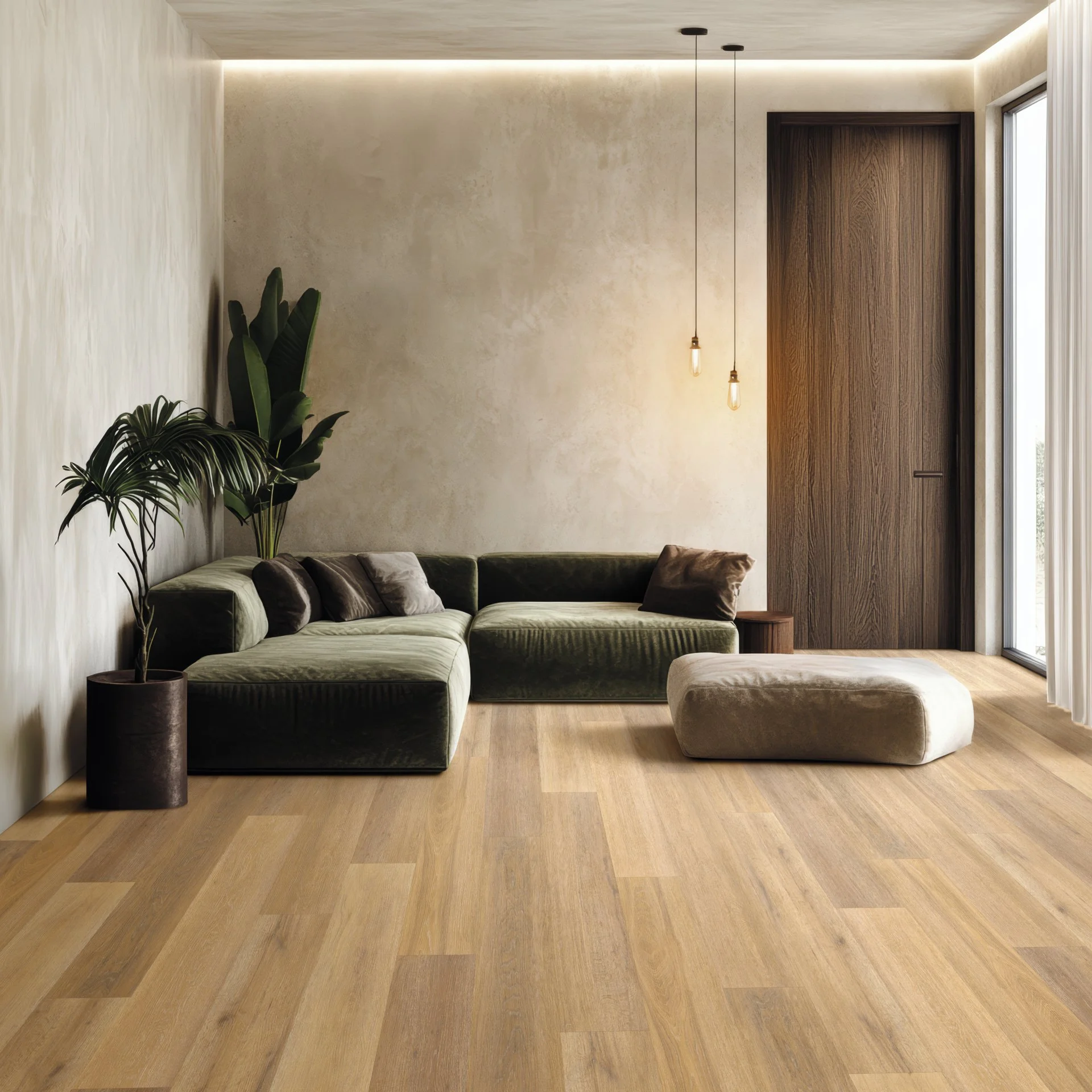 A minimalist living room with a green velvet sectional sofa, a large potted plant, and a beige ottoman on light wood flooring. There are two hanging light bulbs and a wooden door on the right, with a large window covered by white curtains.