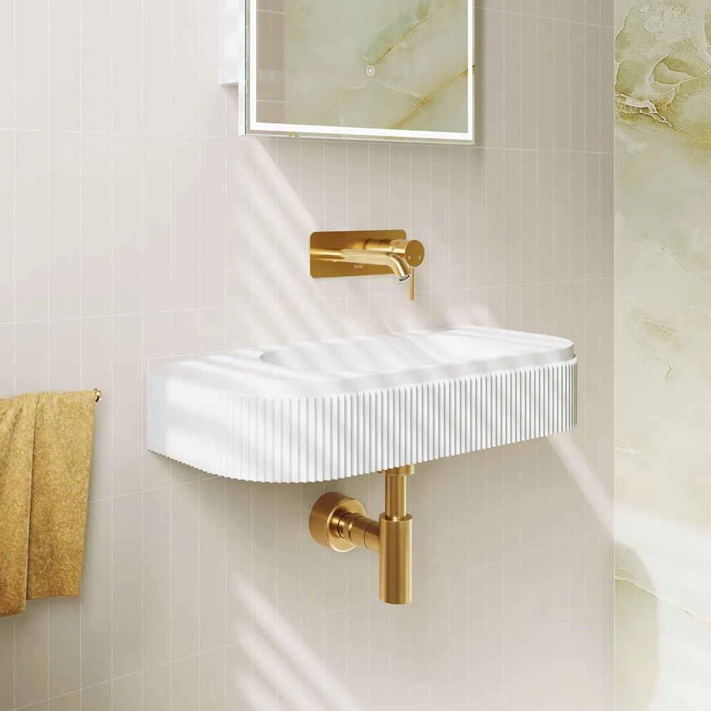 Modern bathroom sink with gold fixtures and a mirror above, beige tiled wall, and a beige towel on a hook.