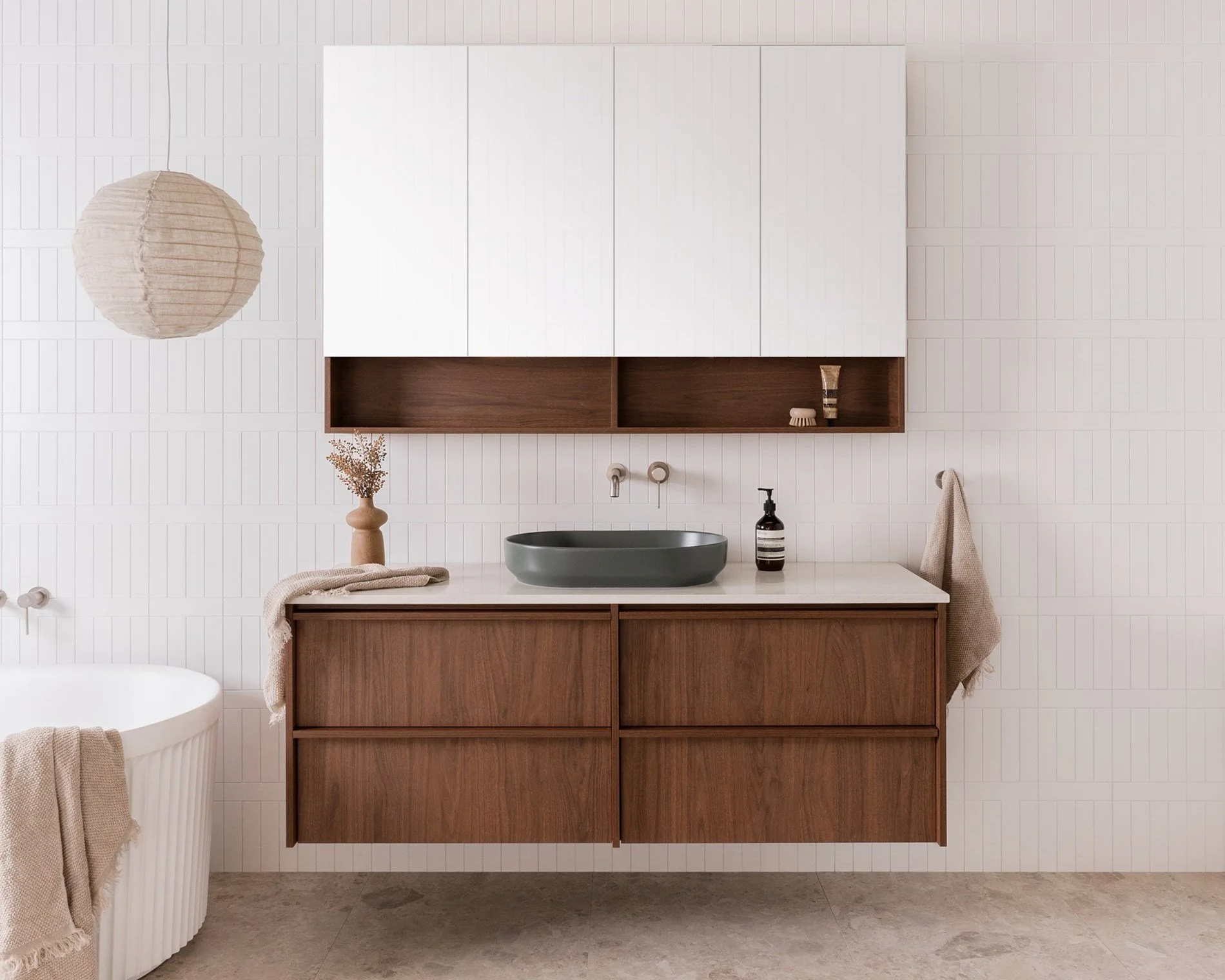 Minimalist bathroom with a floating wooden vanity, a dark green vessel sink, and a wall-mounted faucet. Above the vanity, there is a white cabinet with open shelving in dark wood. To the left, a round beige paper lantern hangs from the ceiling, and a