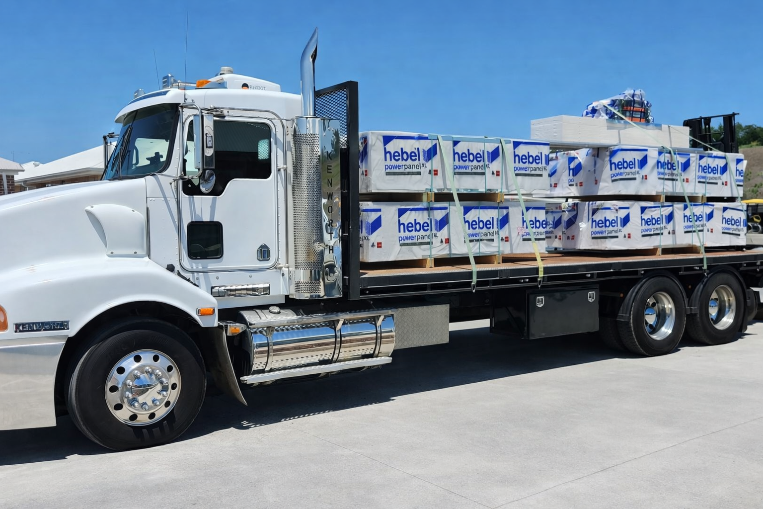 A white flatbed truck loaded with bundles of Hebel power panels on a sunny day.
