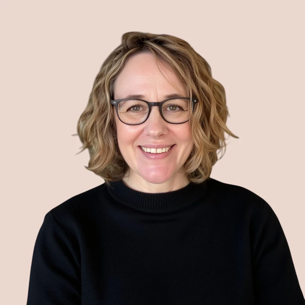 A picture of Emily Wilkinson, with medium length wavy hair, wearing a black sweater and glasses, with a pale pink background..