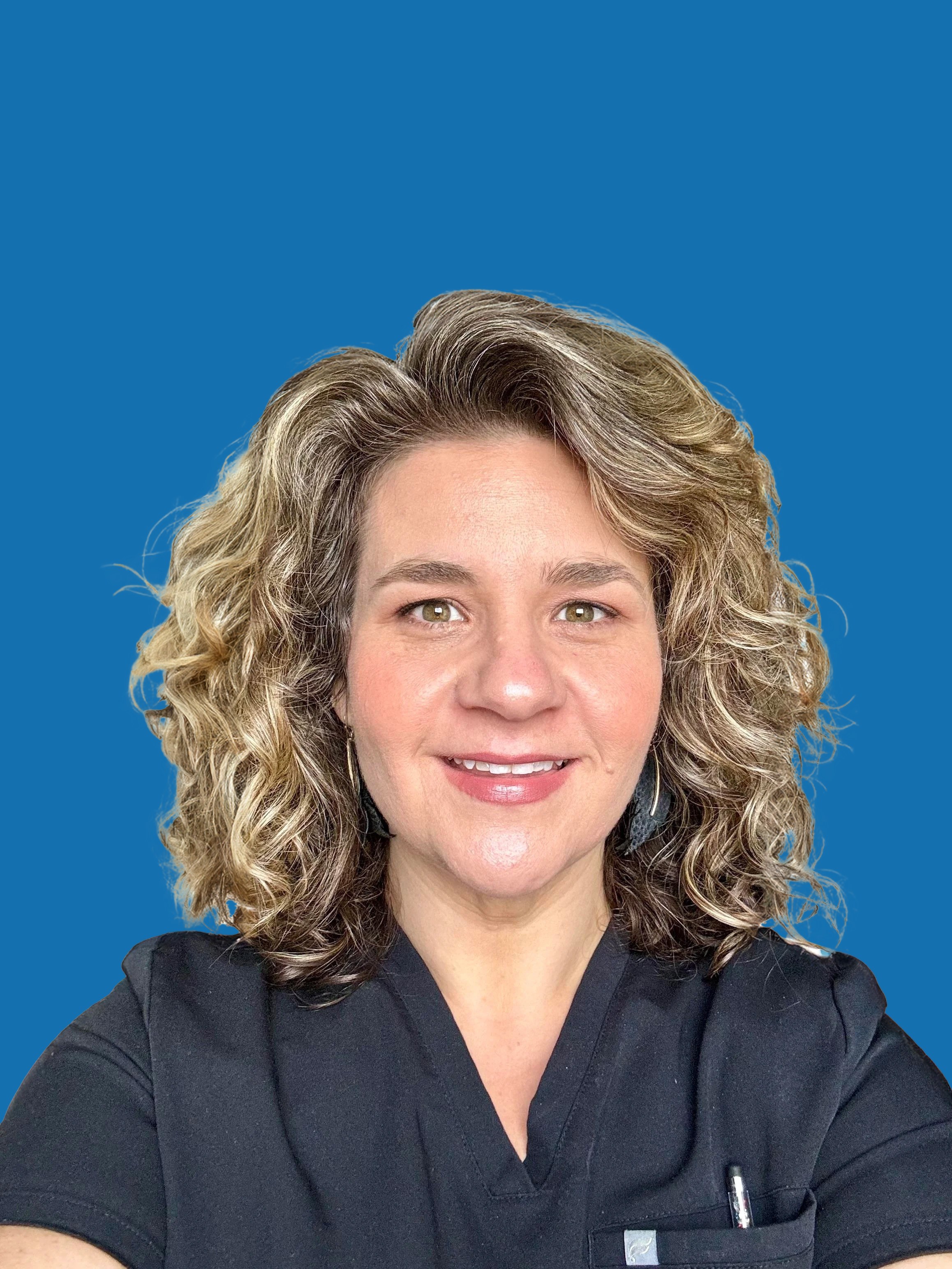 A woman with curly blonde hair and light skin, wearing a black top, smiling against a solid blue background.