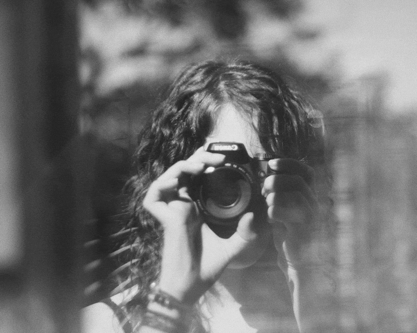A person with curly hair holding a camera, taking a photo.