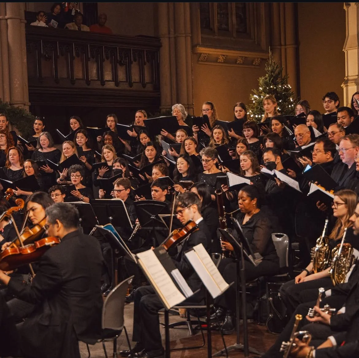 A large choir and orchestra performing in a church or concert hall decorated with a Christmas tree