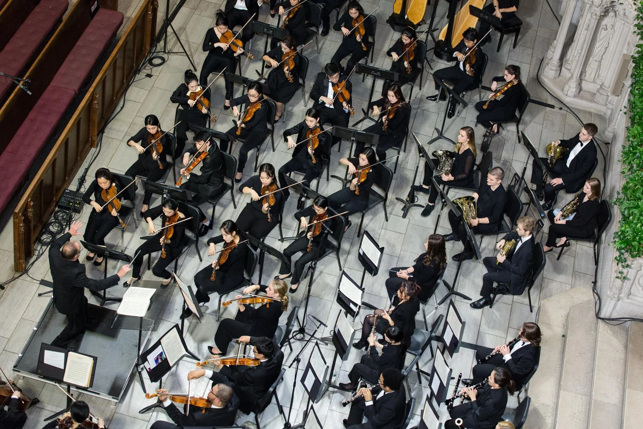 An orchestra performing on stage with musicians playing violins, cellos, and clarinets, conducted by a conductor in a black suit, in a concert hall.