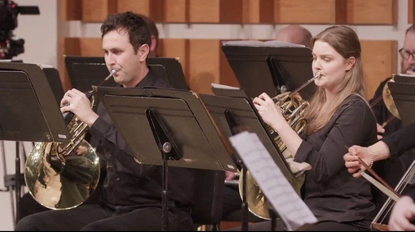 Orchestra musicians playing French horns during a rehearsal or performance.