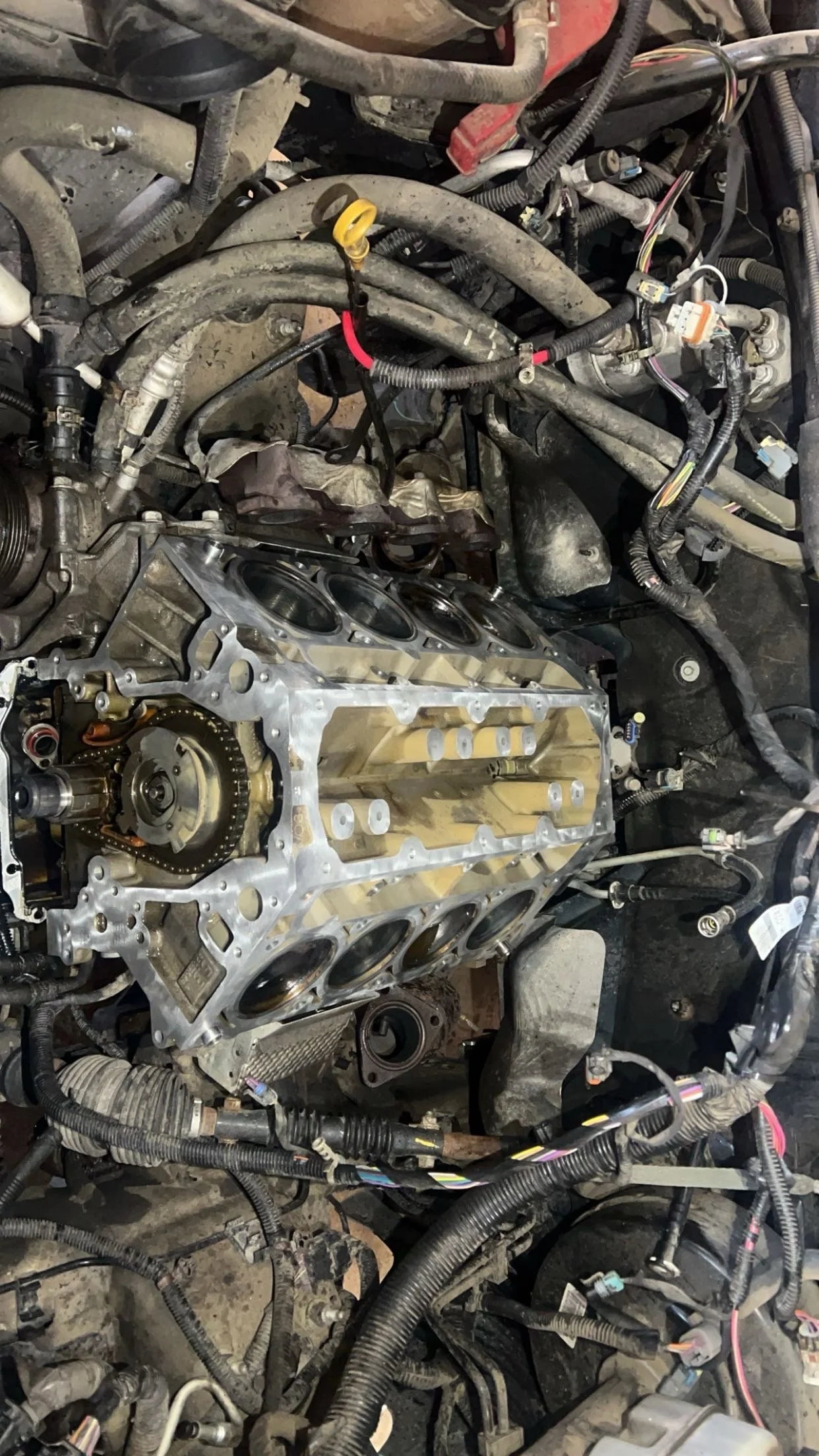 A car engine with the cylinder head removed, exposing pistons inside the engine block, surrounded by various wires and components.