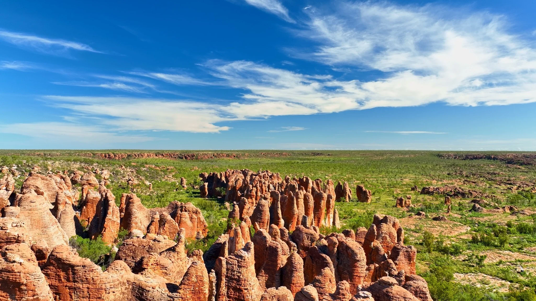 A landscape of rock formations in a desert area with green vegetation, under a blue sky with white clouds.