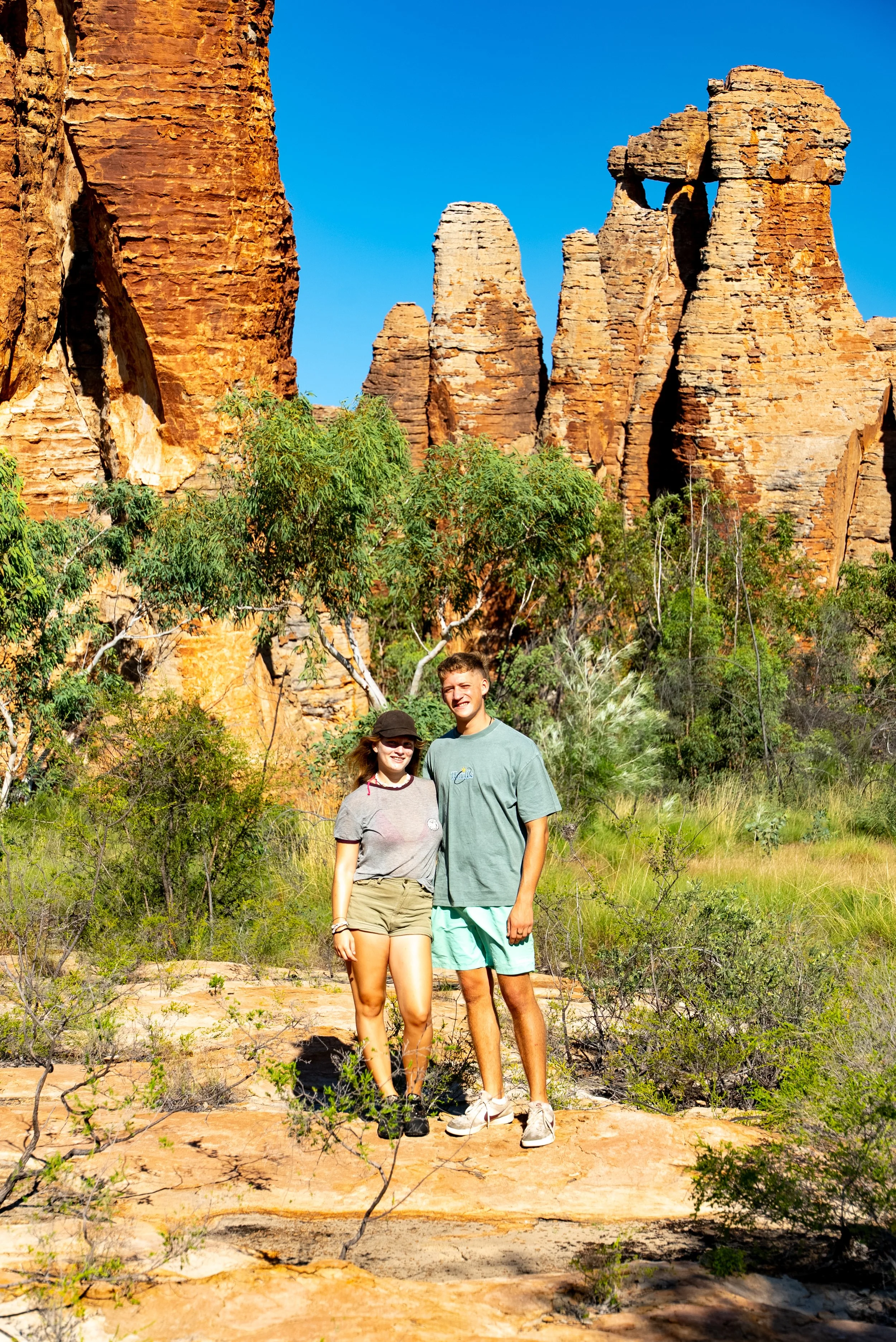Two young people standing in front of desert rock formations and sparse greenery.