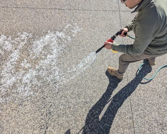 A man using a hose spray gun to clean (sanitise and deodorise) a concrete surface, with cleaning solution spraying from the nozzle.