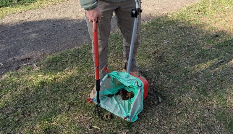 A person scooping dog poop using a pooper scooper tool on a lawn, showcasing the residential Dog Waste Removal service.