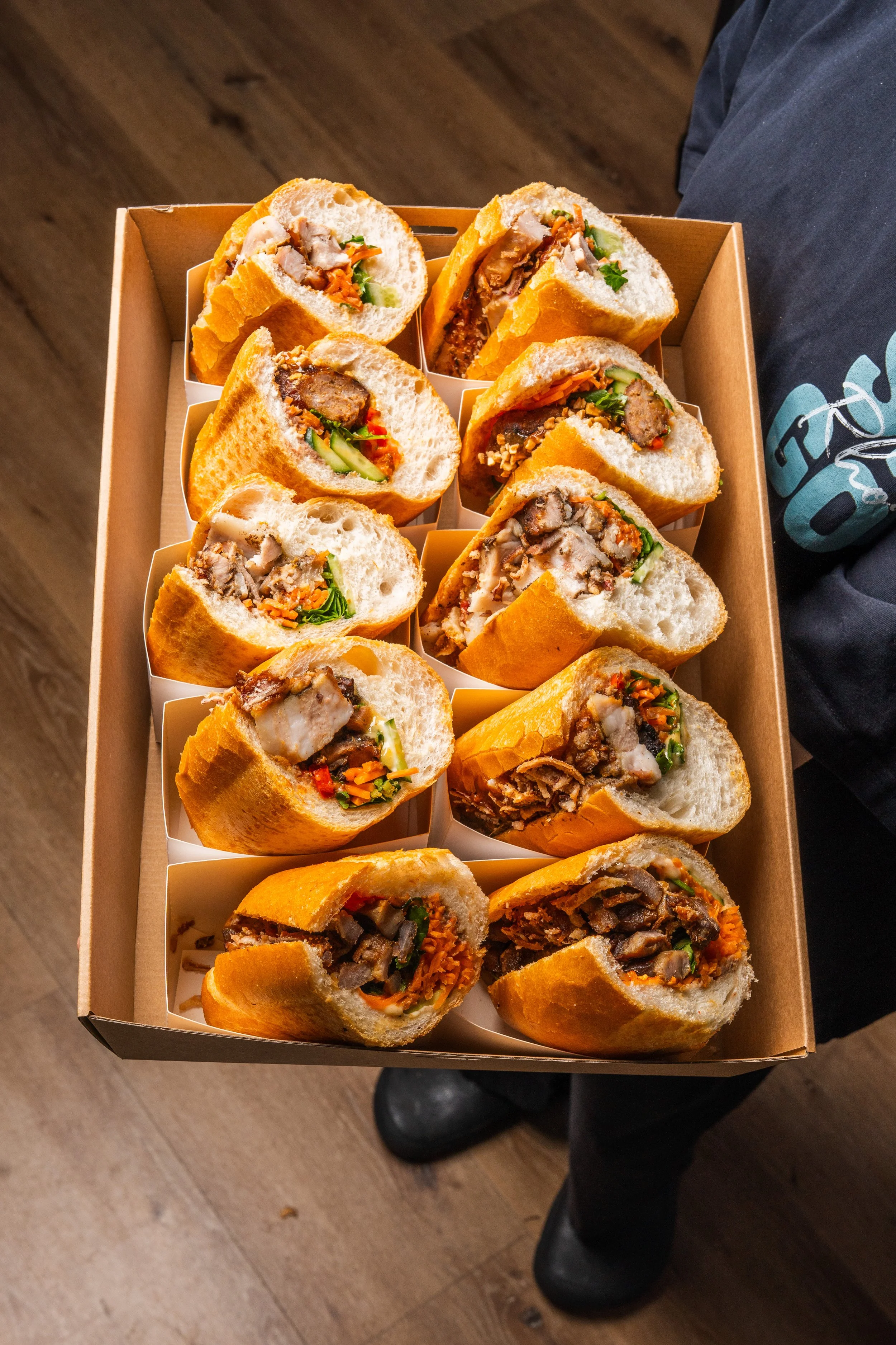 a well-presented catering tray of LA'SEN’s halved banh mi banquettes filled with savoury meat, vegetables, and sauces.