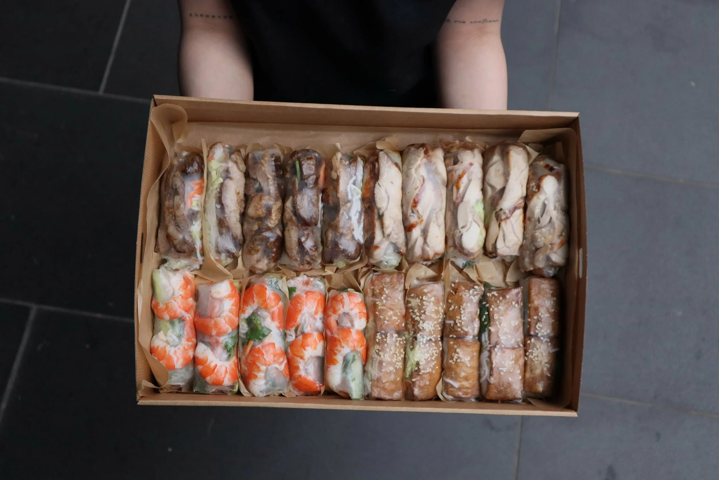 A LA'SEN catering box containing a variety of rice paper rolls featuring prawn, tofu, chicken, and pork.