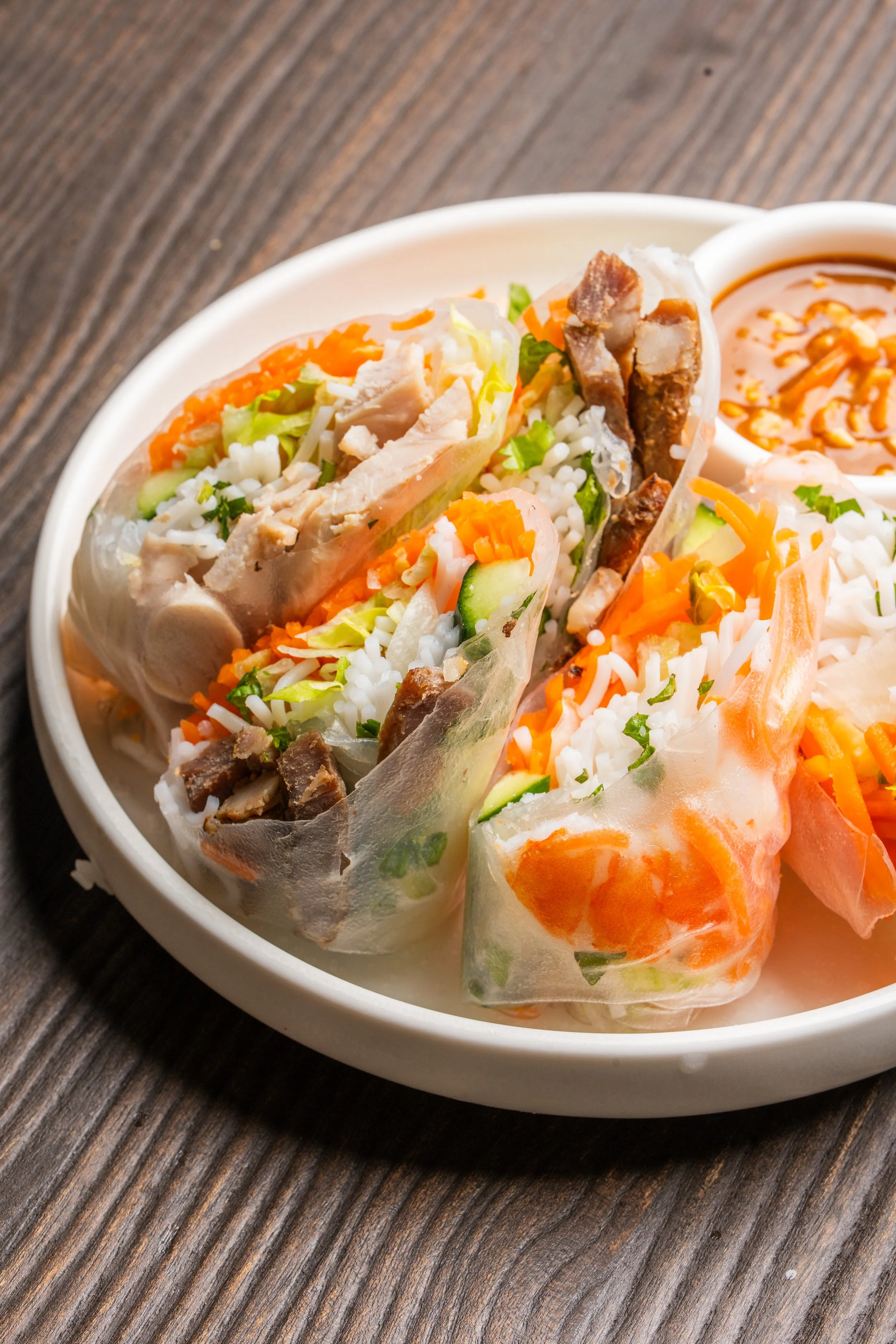 A plate of delicious rice paper rolls containing a variety of meats, vermicelli noodles, and vegetables, accompanied by a rich peanut dipping sauce.