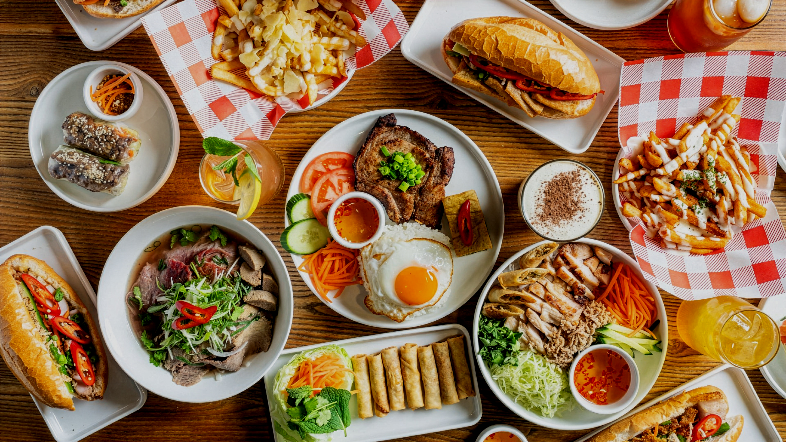 Vietnamese catering spread by LA’SEN Kitchen featuring banh mi, grilled pork, pho, spring rolls, vermicelli bowls, and loaded fries, styled for corporate and event catering.