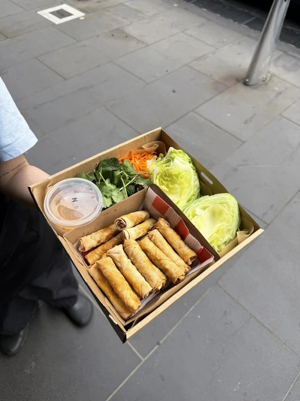 A LA'SEN catering box featuring crispy spring rolls, fresh lettuce, carrot, parsley, and dipping sauce