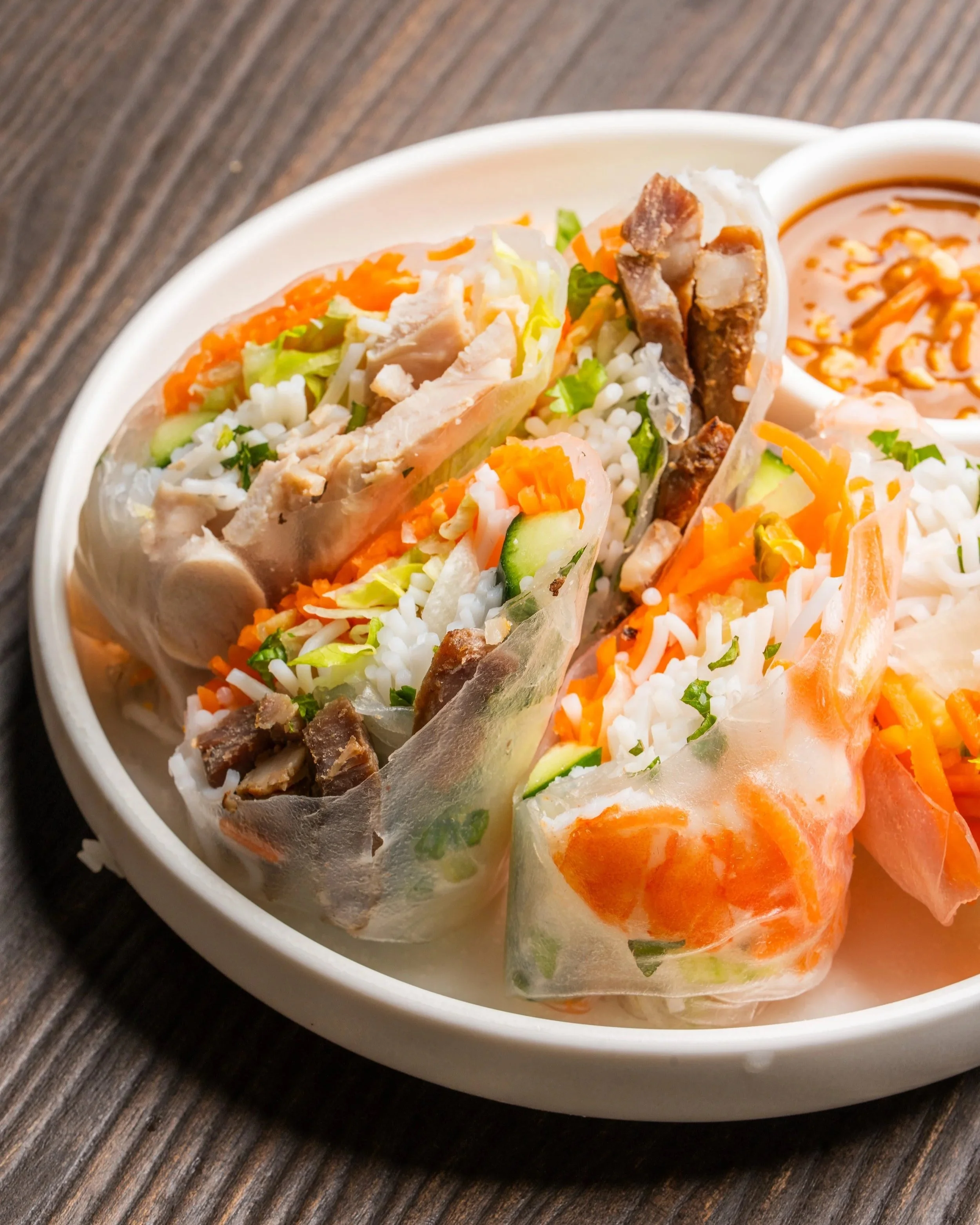 A plate of delicious rice paper rolls containing a variety of meats, vermicelli noodles, and vegetables, accompanied by a rich peanut dipping sauce.