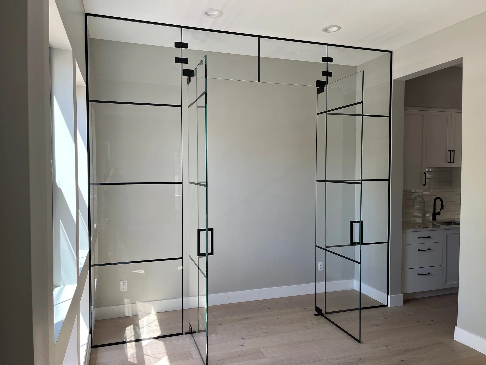 A modern, minimalist glass room divider with black metal frame in a bright kitchen area.