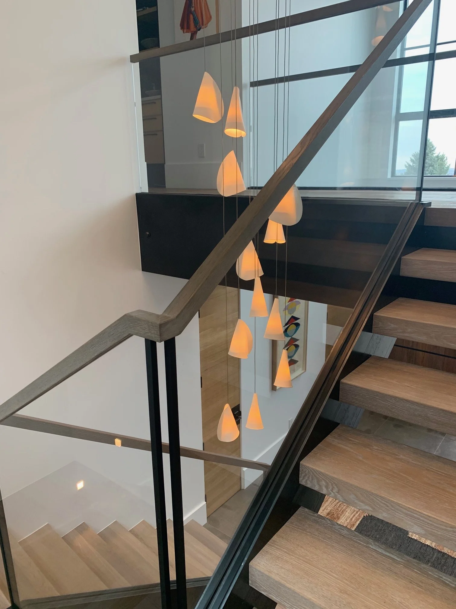 Modern staircase with glass railing, wooden steps, and a hanging pendant light fixture with multiple warm-tone cone-shaped shades.