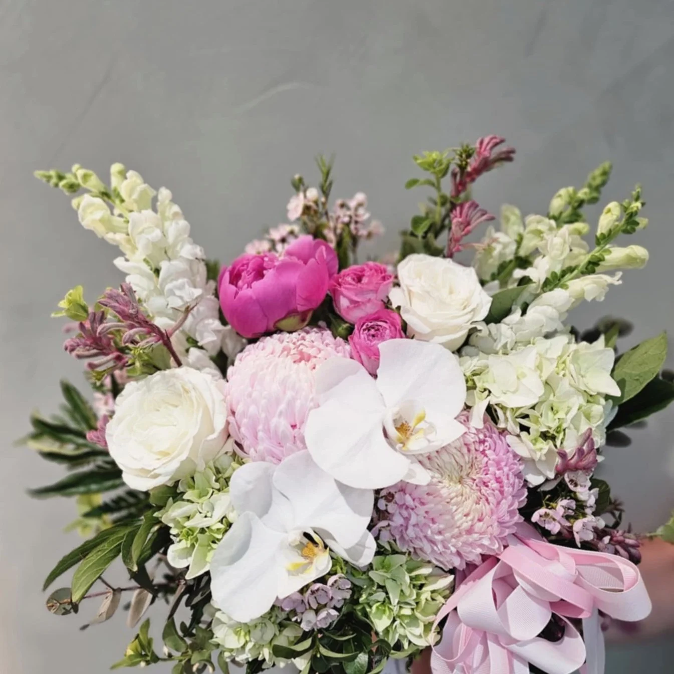 A bouquet/ centerpiece of pink, white, and purple flowers, including orchids and roses, with a pink ribbon.