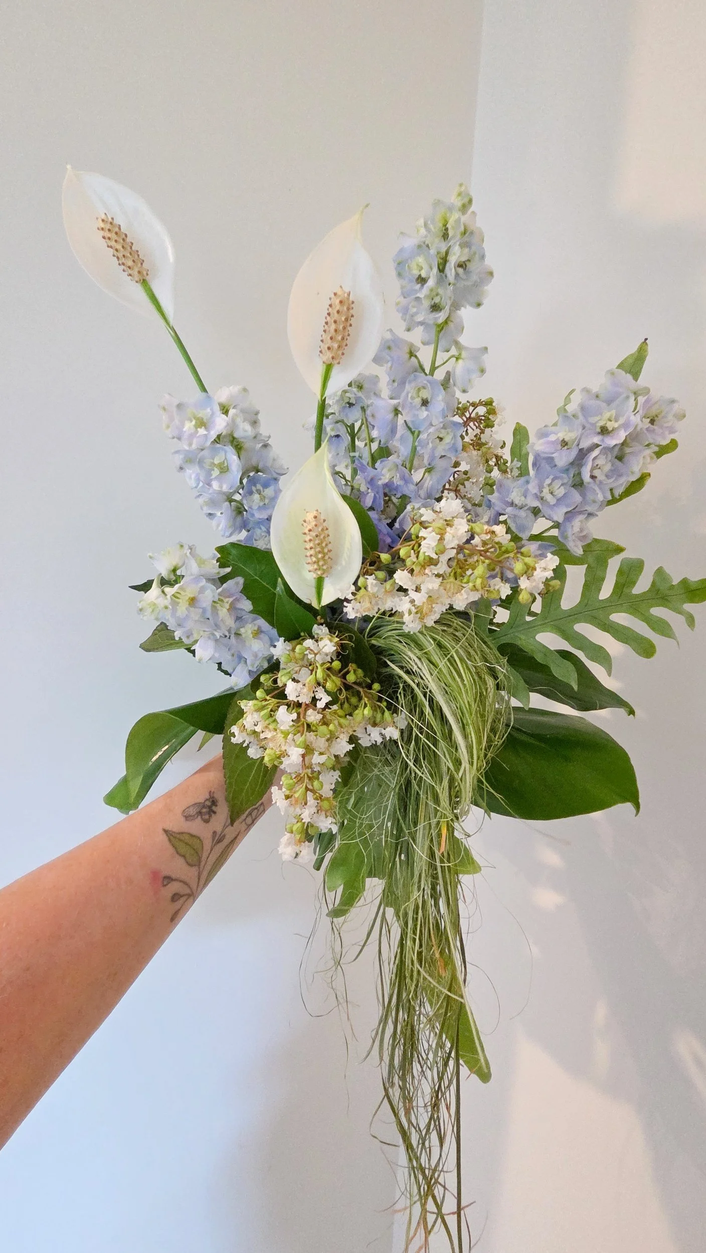 A bridal bouquet of pale blue delphinium, textured greenery and white peace lilly