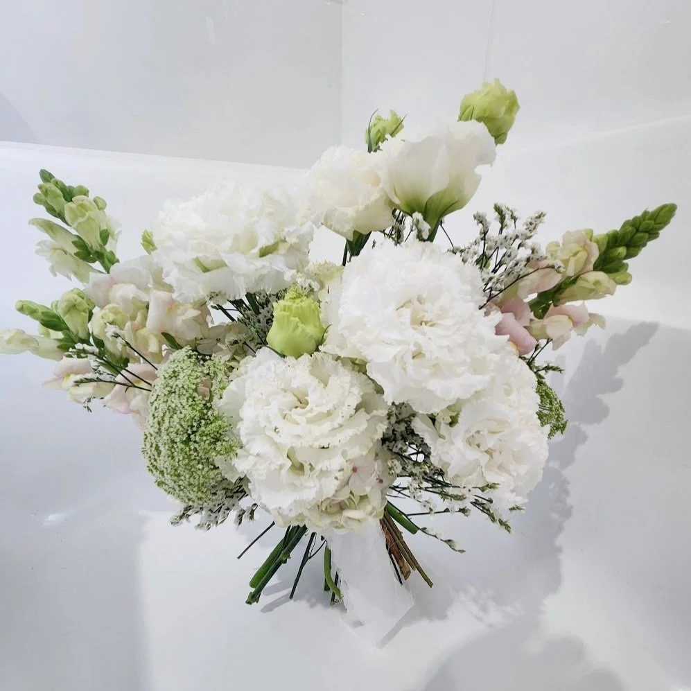A bouquet of white roses, carnations, and other white flowers with green eucalyptus leaves against a gray background.