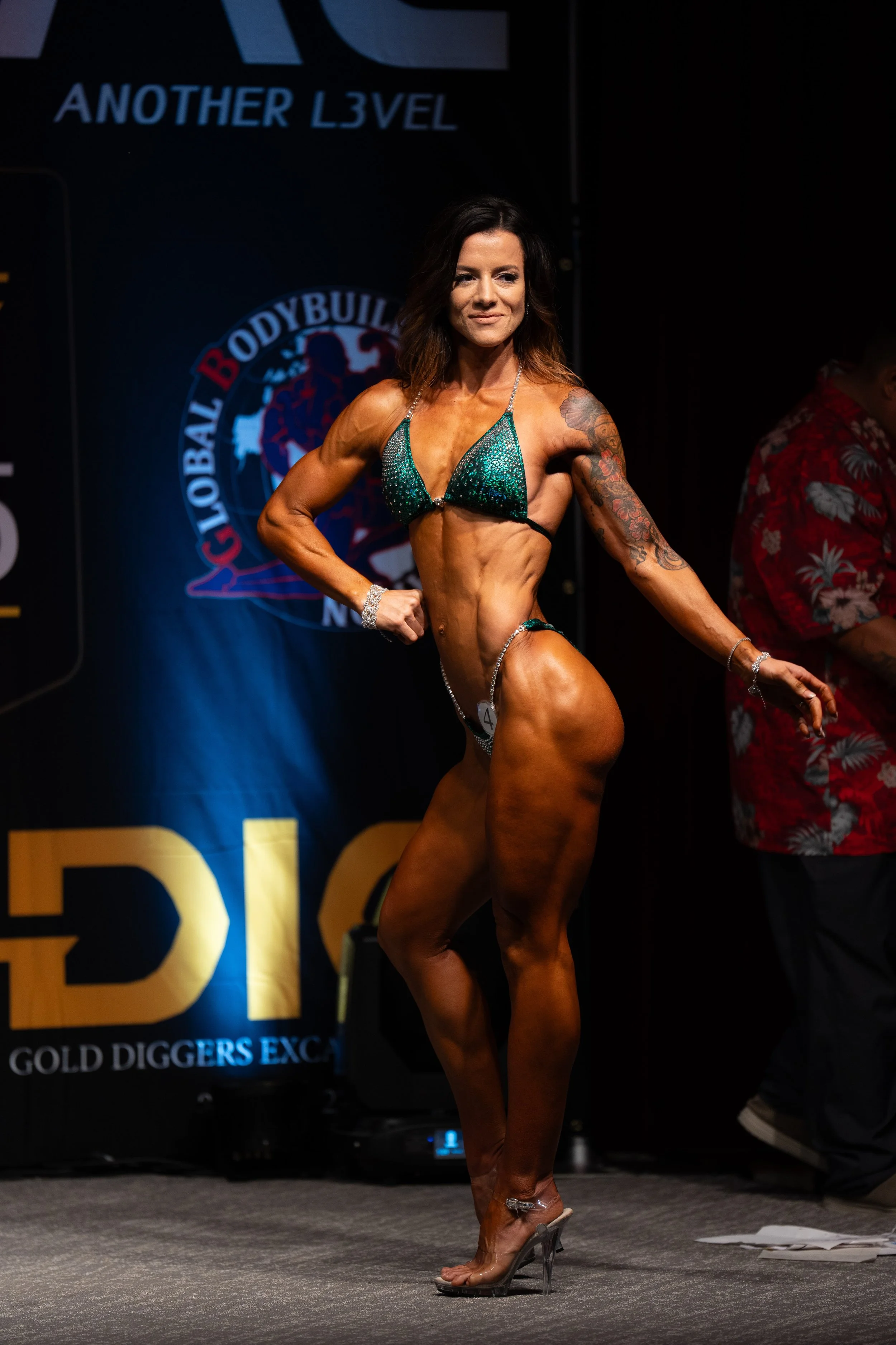 A female bodybuilder in a green bikini posing on stage during a competition.