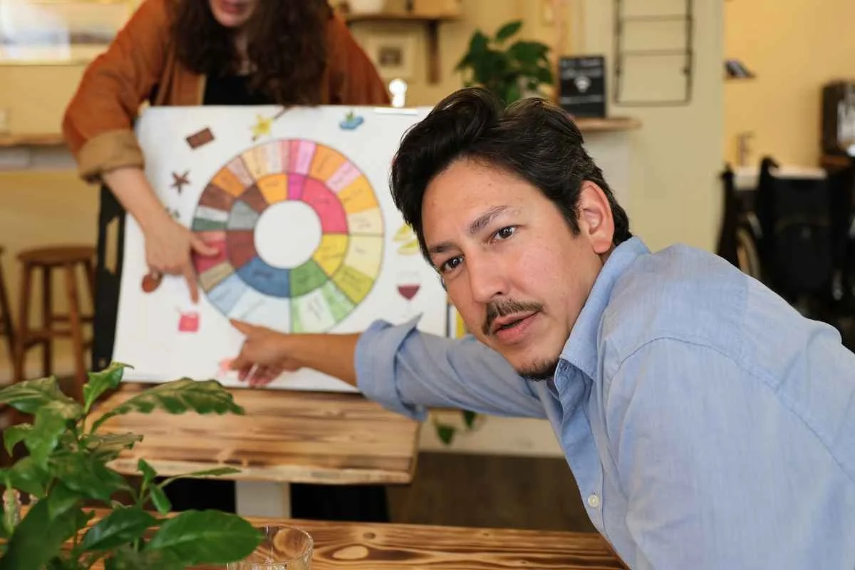 Two women tasting coffee from black cups on a wooden table in a cozy room.