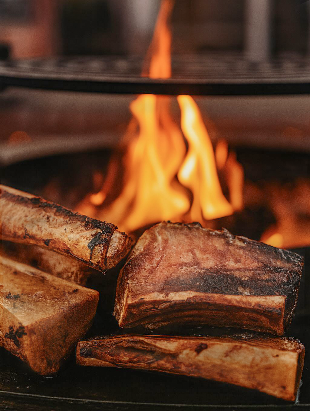 Close-up of raw beef steaks and pork ribs cooking over an open flame on a grill.