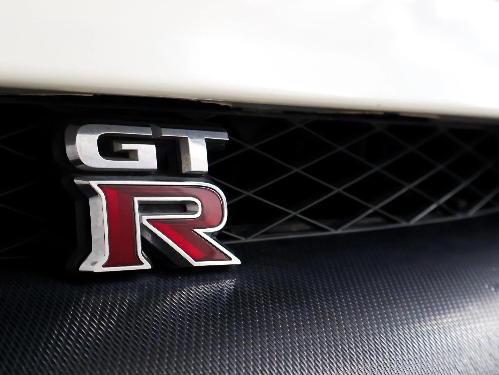 Close-up of a car badge with the letters GT R in silver, black, and red, mounted on a black grille.