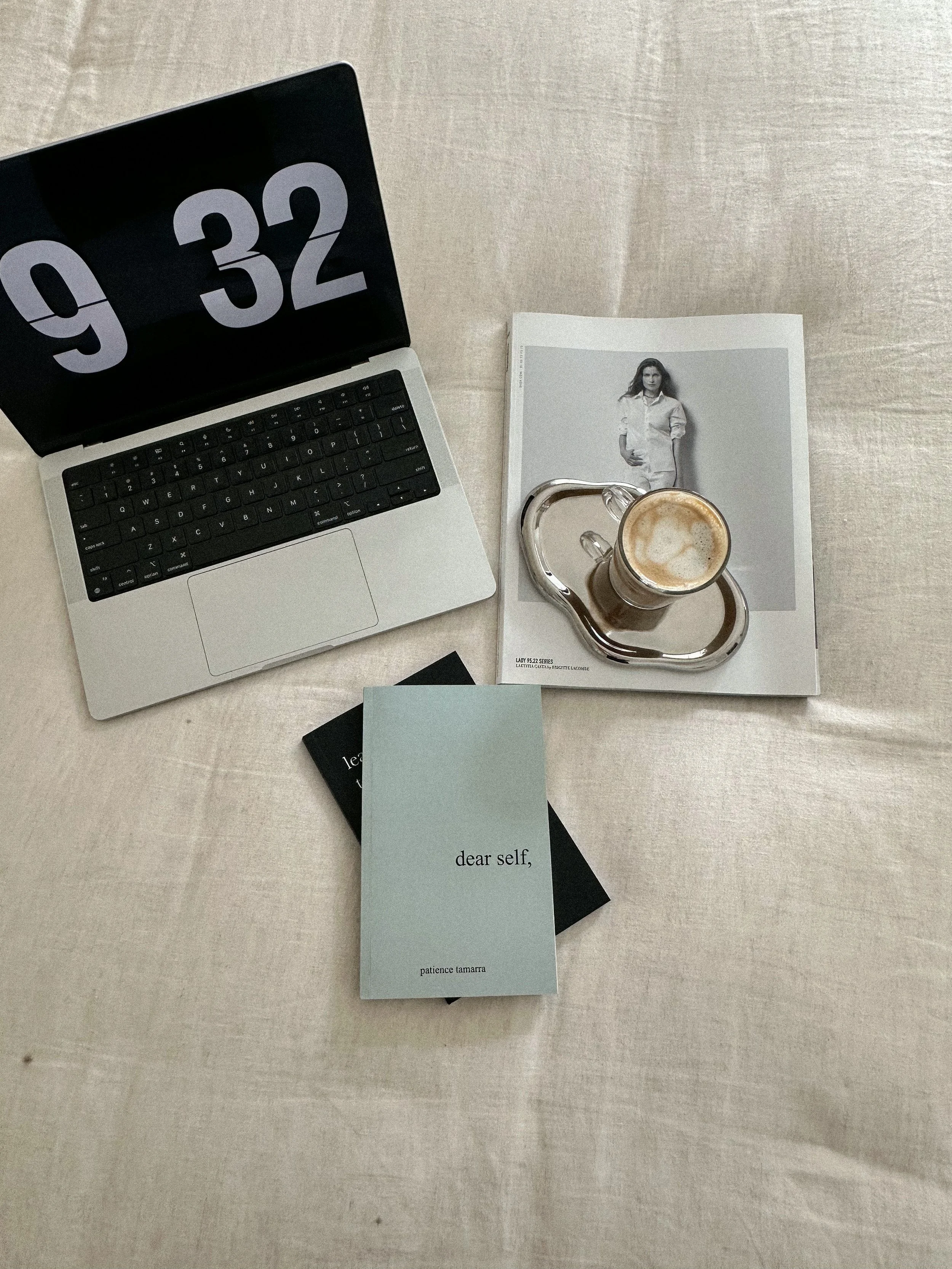 Woman with long dark hair wearing a pink shirt sitting at a desk with open books, a pair of glasses, a white mug, and a tablet, appearing to study or work.