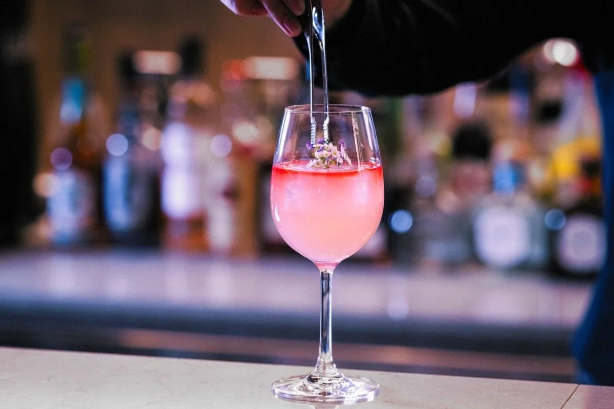 A bartender garnishing a pink cocktail with flowers in a wine glass.