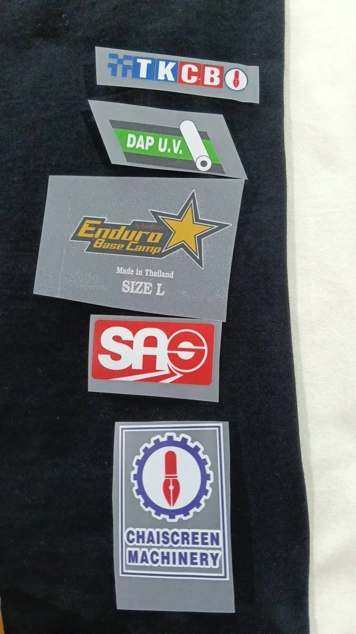 Collection of various stickers on fabric, including tech company logos, a construction company sticker, a camping gear logo, a logo for SAS, and a machinery company logo.