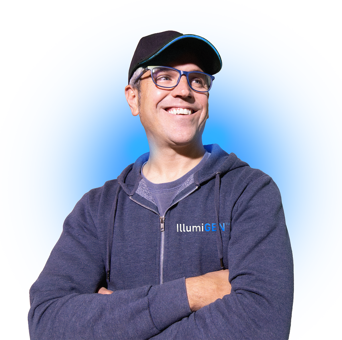 A man smiling with arms crossed, wearing glasses, a black cap, and a dark gray hoodie with 'IllumiGEN' written on it, against a blue background.